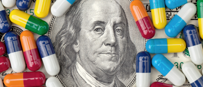 Colourful prescription capsules scattered across a U.S. $100 bill around Benjamin Franklin’s portrait.