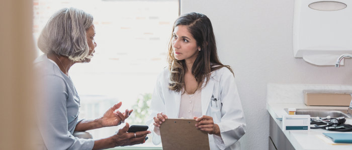 Female doctor holding clipboard listens to older woman during consultation.