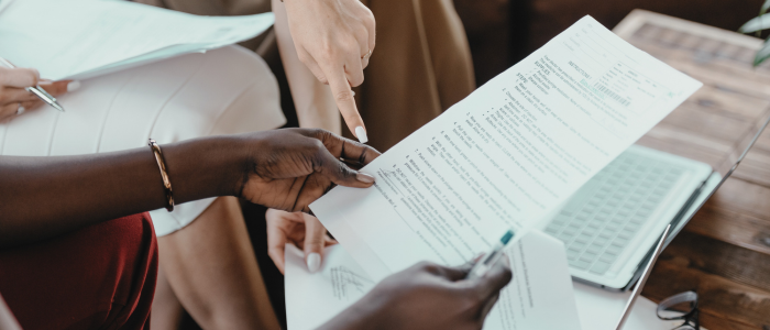 Two people review and discuss a printed report beside an open laptop. To represent that a new report explores health technology assessment body and regulator collaborations to address evidence challenges and uncertainty for timely patient access. 