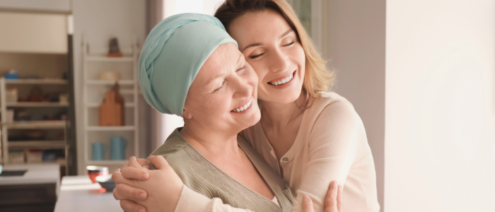 Smiling woman wearing a headscarf embraces another smiling woman indoors, to represent that Guardant Health and ConcertAI to advance cancer research with multi-modal RWD platform.