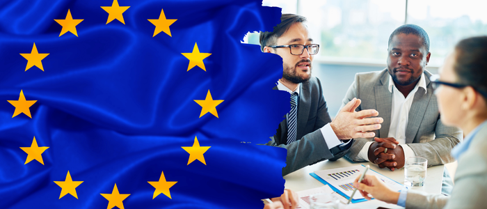 EU flag beside business professionals discussing documents at a meeting table.
