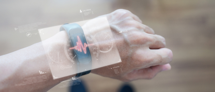 Hand wearing a smart fitness band displaying a futuristic holographic interface with heart rate monitoring, health metrics, and data visualisations, representing wearable-based endpoints in clinical research.