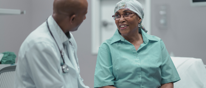 Doctor talks with smiling cancer patient wearing headscarf in exam room.