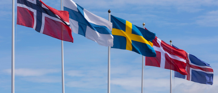 Flags of Norway, Finland, Sweden, Denmark, and Iceland flying on flagpoles against a blue sky.
