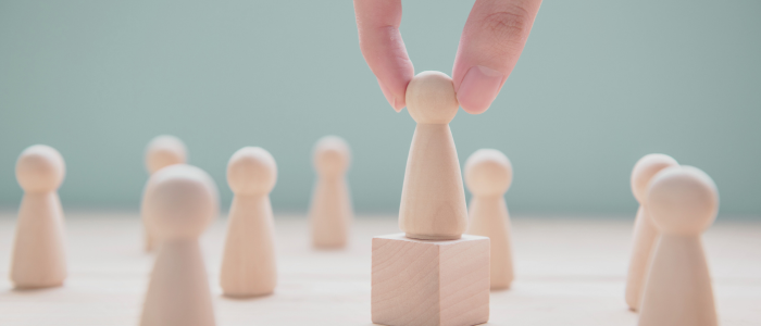 Hand lifts one wooden figure above others, symbolizing focus on an individual with a rare disease.