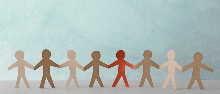 Paper cutout figures hold hands in a row, with one red figure standing out among neutral tones. To represent 'Navigating access challenges for rare diseases: stakeholder insights'. 
