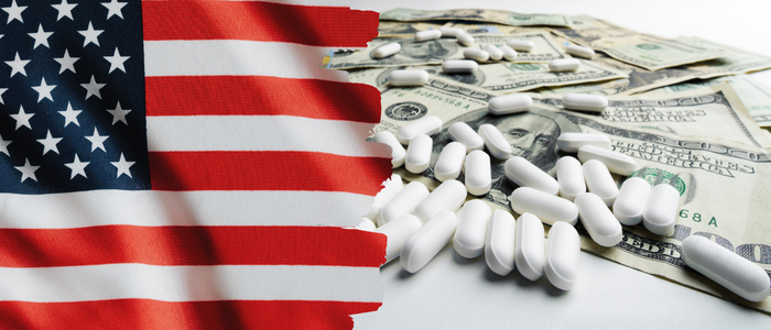US flag beside piles of white pills scattered over US dollar banknotes.