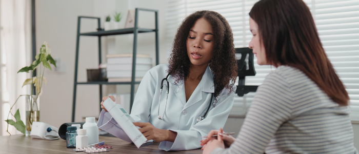 Doctor showing a form to a patient at a desk; medical supplies on the table in a clinic office.