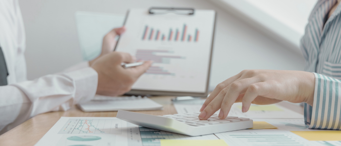 Two people reviewing financial documents, with one using a calculator and the other holding a clipboard displaying charts