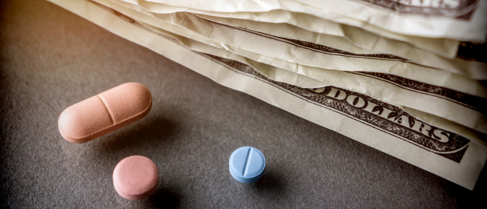 Prescription pills and US dollar bills on a table, illustrating the legal challenge to the GLOBE drug pricing rule and debate over QALY-based benchmarks.