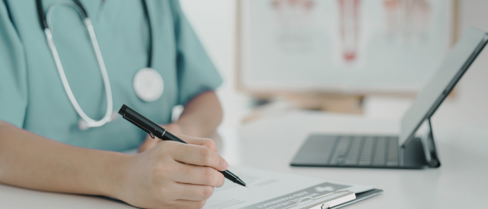 Doctor writes on clipboard beside tablet in medical office.