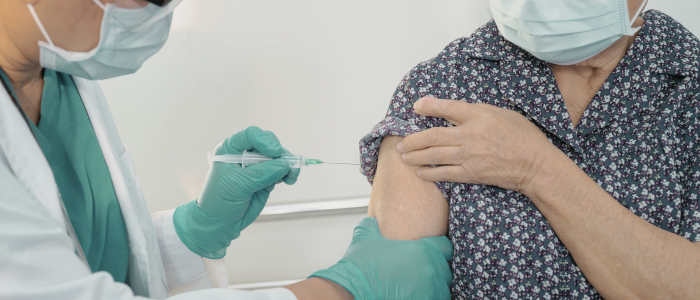 Healthcare worker administers vaccine to elderly patient wearing a mask.