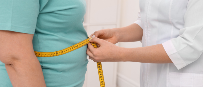 A healthcare professional measures a person’s waist with a yellow tape measure over a teal shirt.