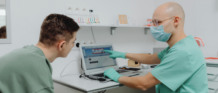 A masked clinician points to images on a laptop while a patient leans in to look.