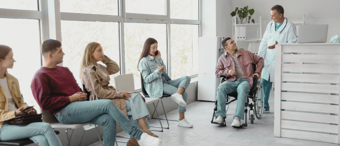 Patients sit in a clinic waiting room while a doctor talks to a man in a wheelchair.