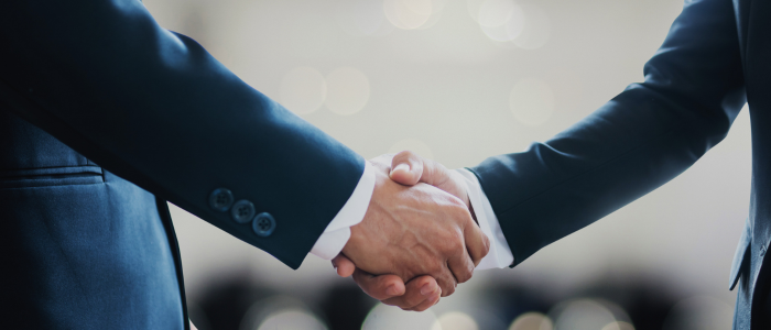 Two people in suits shake hands in a business setting.