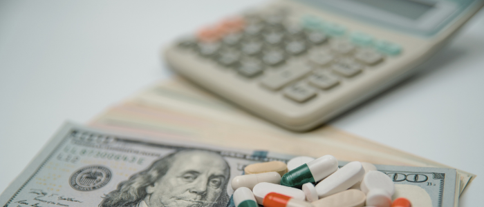 Mixed capsules placed on top of dollar bills beside a calculator, suggesting healthcare expenses
