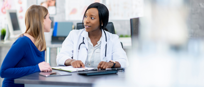 Doctor with stethoscope discusses medical information with a patient seated across a desk.