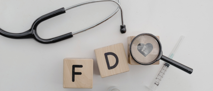 Wooden blocks spelling “FDA” with a stethoscope, syringe, and magnifying glass highlighting a heart symbol, representing the FDA’s role in healthcare oversight and regulatory decisions.