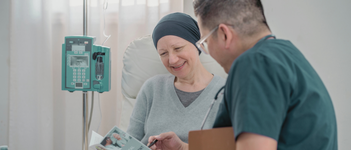 Nurse reviews pamphlet with smiling cancer patient receiving IV treatment.