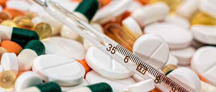 Mixed pills and capsules scattered with a glass needle lying on top.
