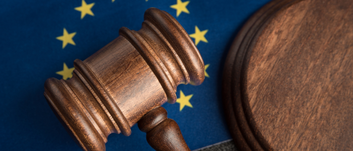 Wooden judge's gavel and sound block resting on an EU flag with yellow stars on a blue background.