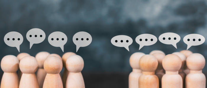 Wooden peg figures in two groups facing each other with speech bubble icons above them, representing dialogue and collaboration between organizations.