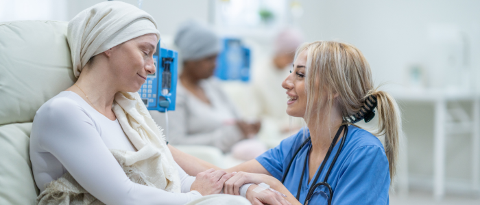 Nurse in blue scrubs comforts a patient wearing a headscarf during chemotherapy treatment in an oncology clinic.