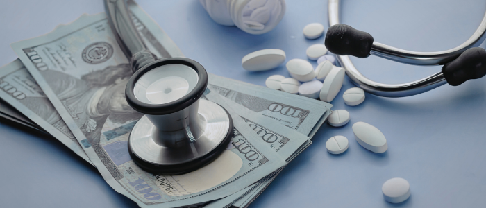 Stethoscope and prescription pills resting on US dollar banknotes, on a light blue background.