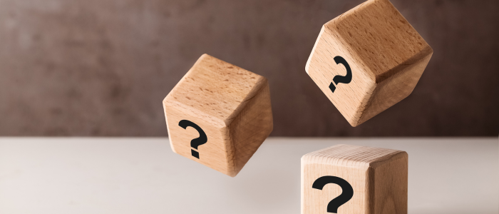 Three wooden blocks with question marks, shown in mid‑air, representing uncertainty in decision-making.