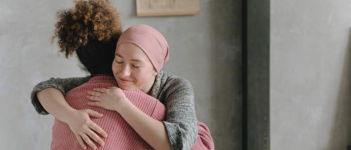 A woman in a pink headscarf hugs another woman in a pink sweater, smiling with closed eyes. To represent that Flatiron Health and Exact Sciences drive innovation in MRD testing through RWE.