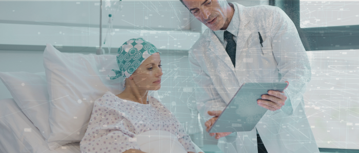 Doctor shows tablet to hospitalized cancer patient wearing headscarf, with digital data overlay.