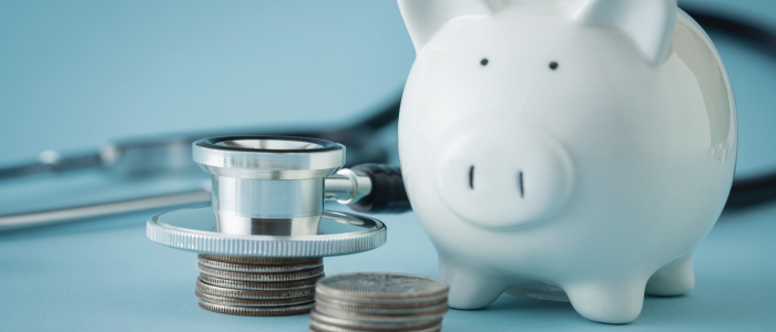 A stethoscope resting on a pile of coins, next to a piggybank.