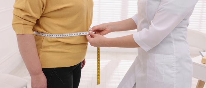 Healthcare professional measures a patient’s waist with a tape measure during a weight management assessment.