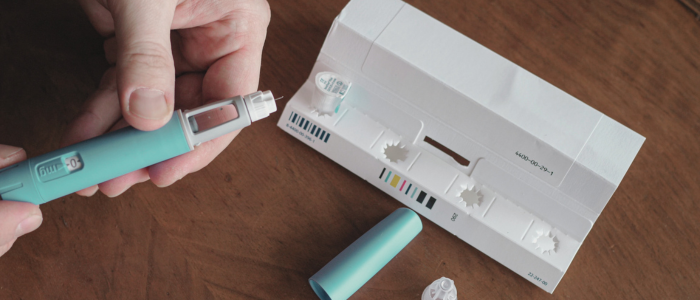 Person holds GLP-1 injection pen beside opened packaging on wooden table.