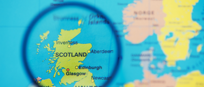 Magnifying glass highlighting Scotland on a map of the United Kingdom, with Glasgow, Edinburgh, and Aberdeen labeled.