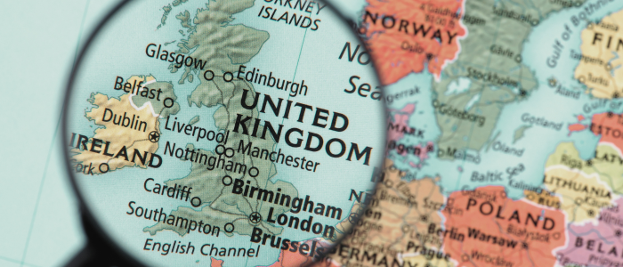 Magnifying glass highlighting the United Kingdom on a printed map of Europe, with surrounding countries visible.