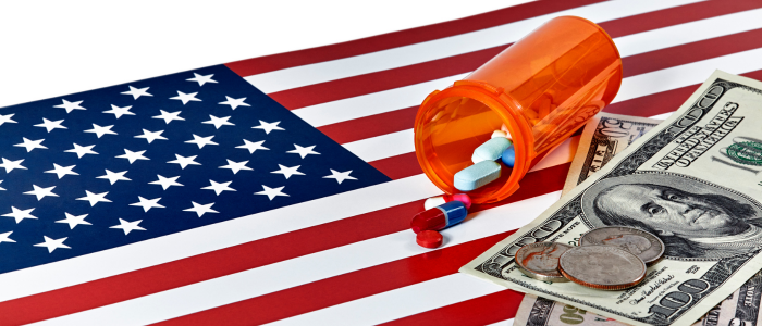 Prescription pill bottle with capsules spilling onto an American flag alongside US dollar bills and coins, representing drug pricing policy