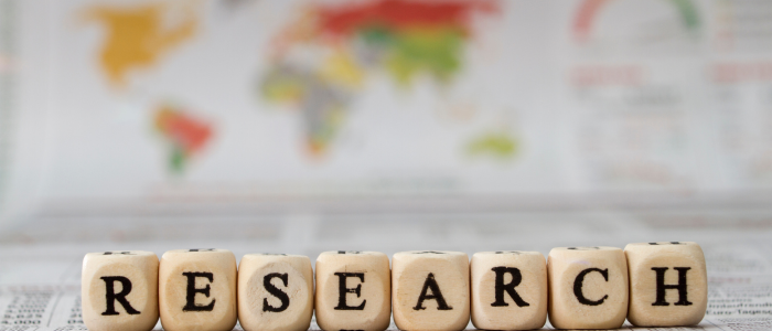 Wooden letter blocks spelling the word “RESEARCH” placed in front of a blurred world map, symbolising global collaboration and international data sharing in inflammatory bowel disease research